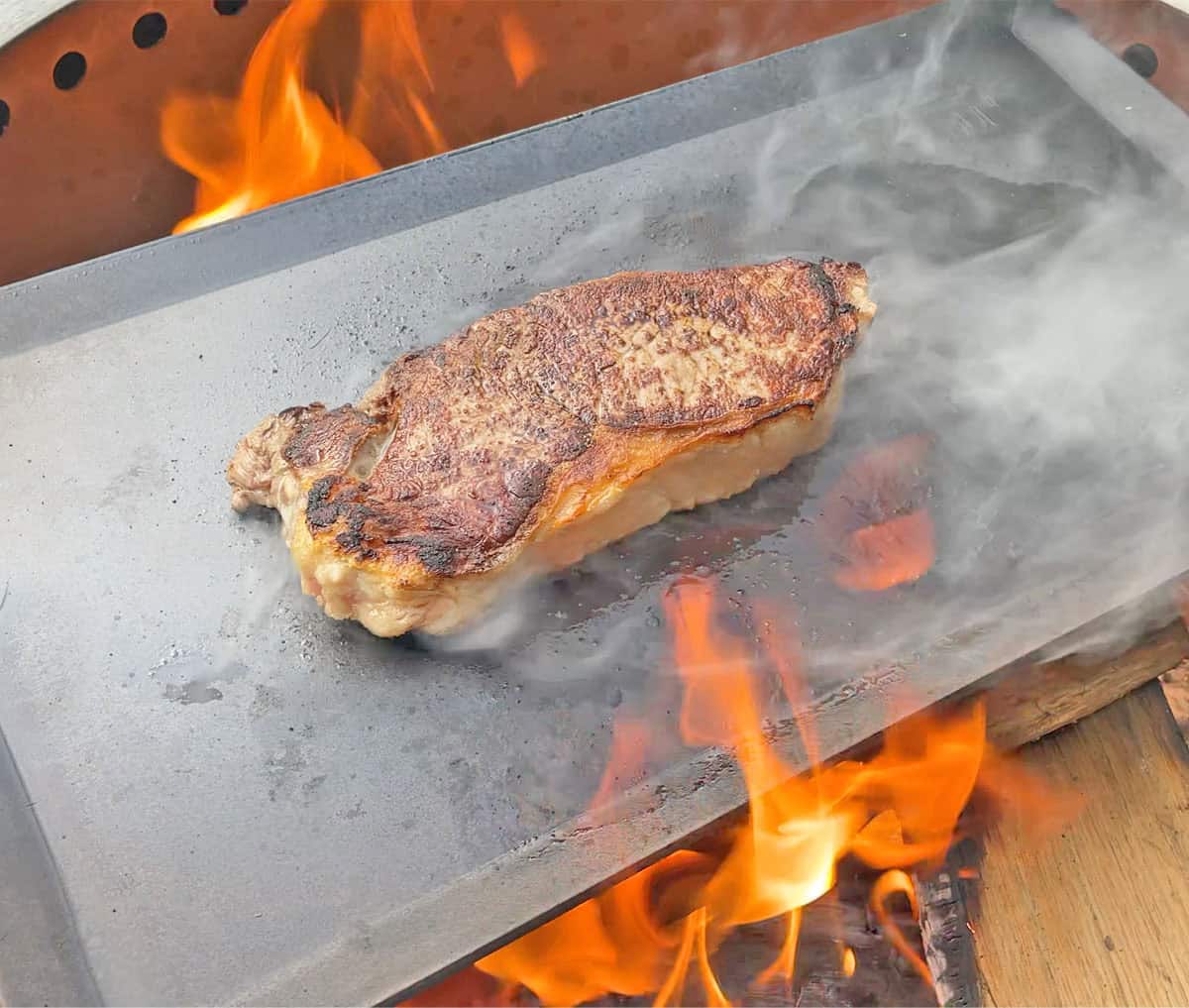 Cooking a steak on the Made In carbon steel griddle over an open flame