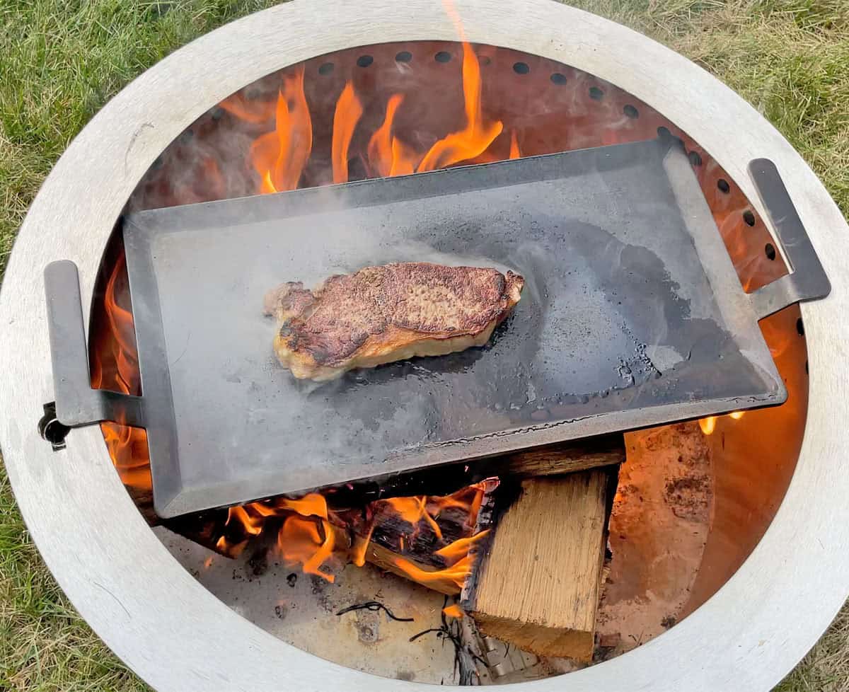 Cooking steak on Made In Carbon Steel Griddle over an open flame