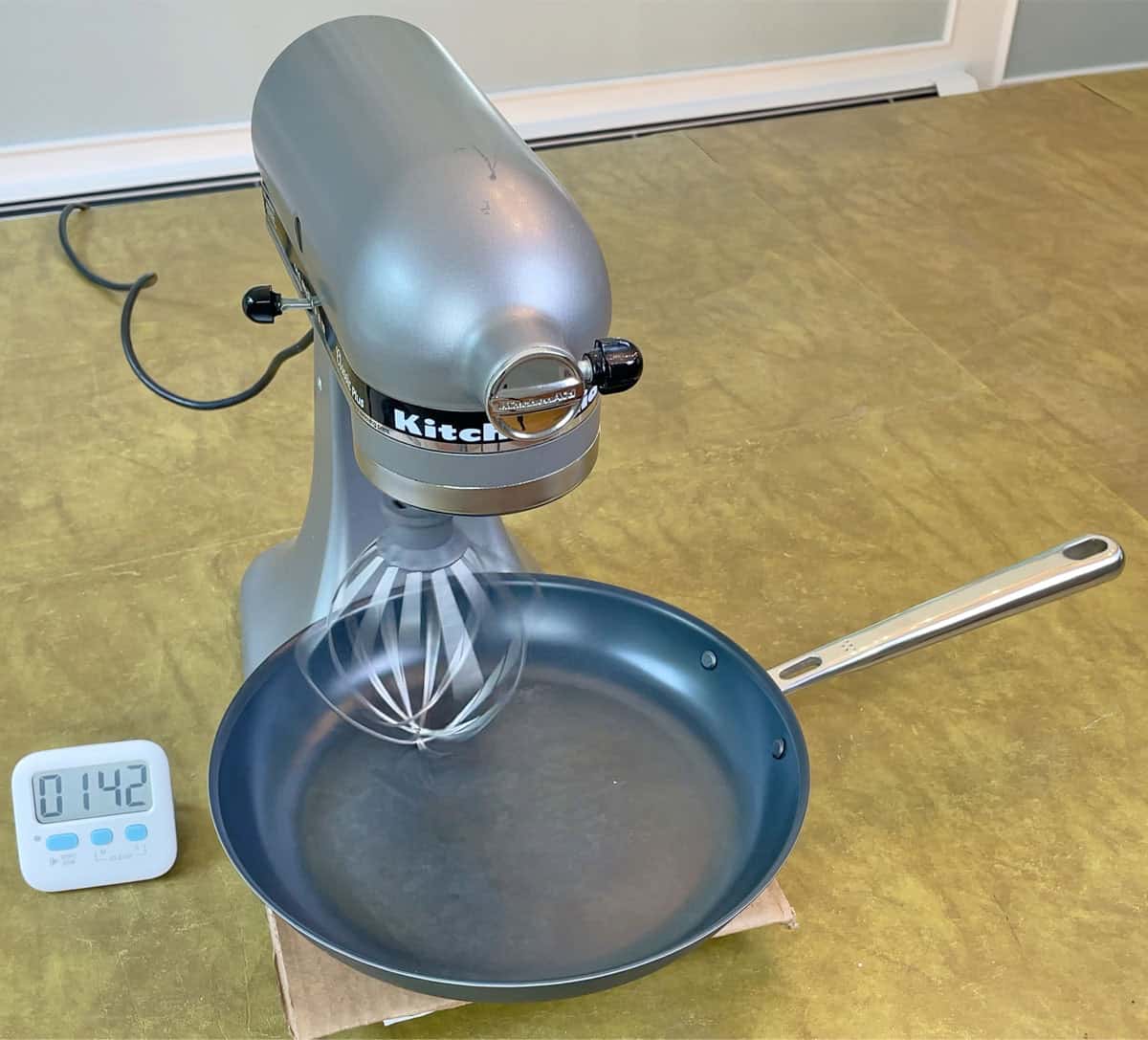 Testing the durability of the Misen Carbon Nonstick pan by scratching it with a metal whisk attachment on a stand mixer