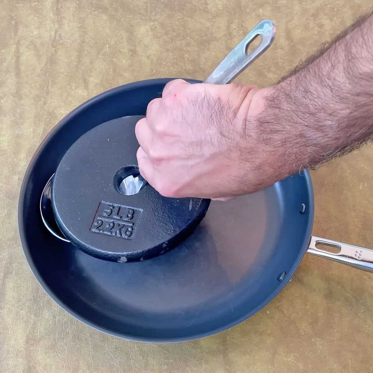 Testing the durability of the Misen Carbon Nonstick pan by scratching it with a weighted metal ladle