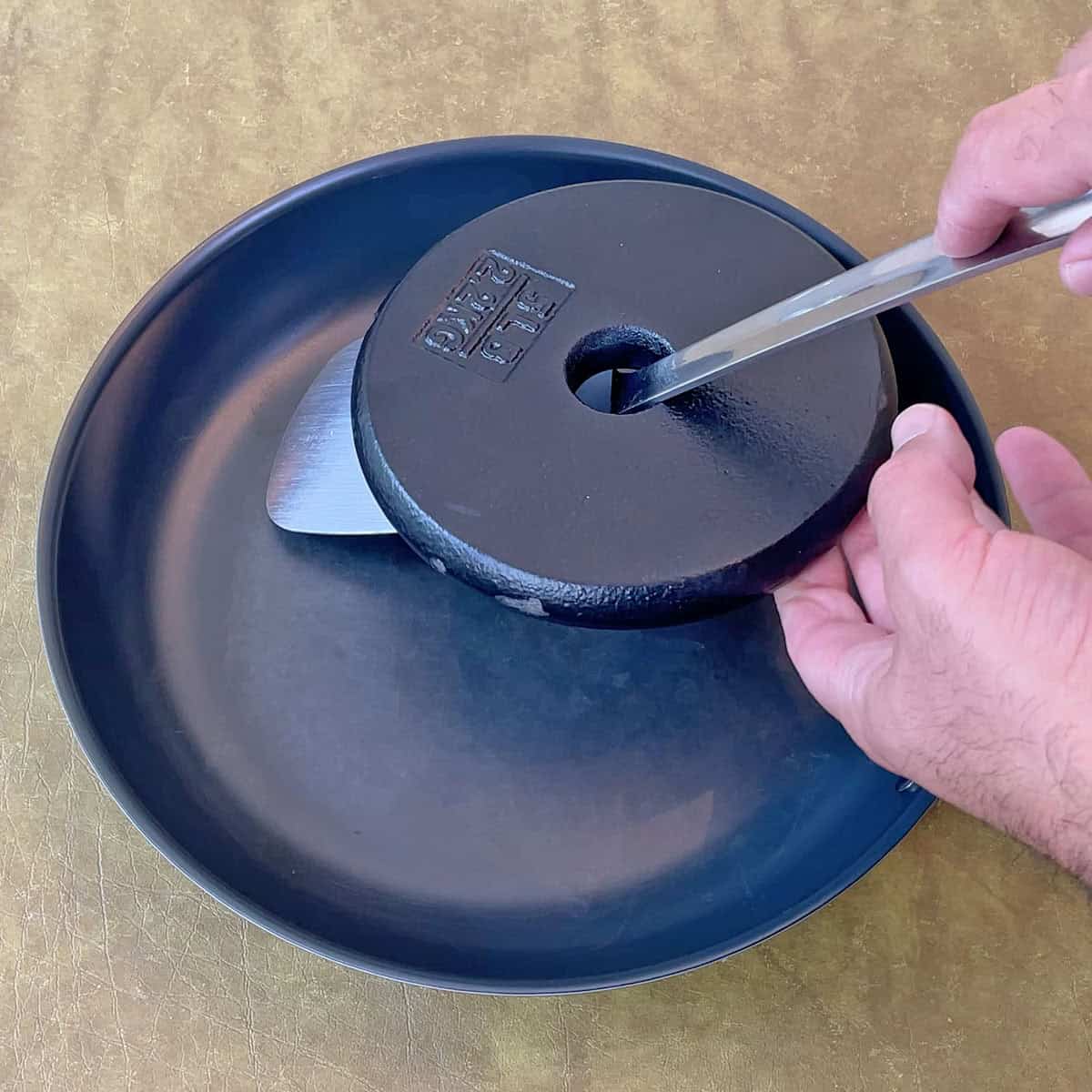 Testing the durability of the Misen Carbon Nonstick pan by scratching it with a weighted metal spatula